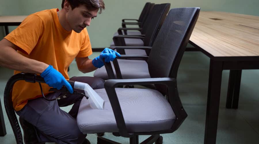 Hard-working janitor is deep-cleansing chairs with vacuum-cleaner